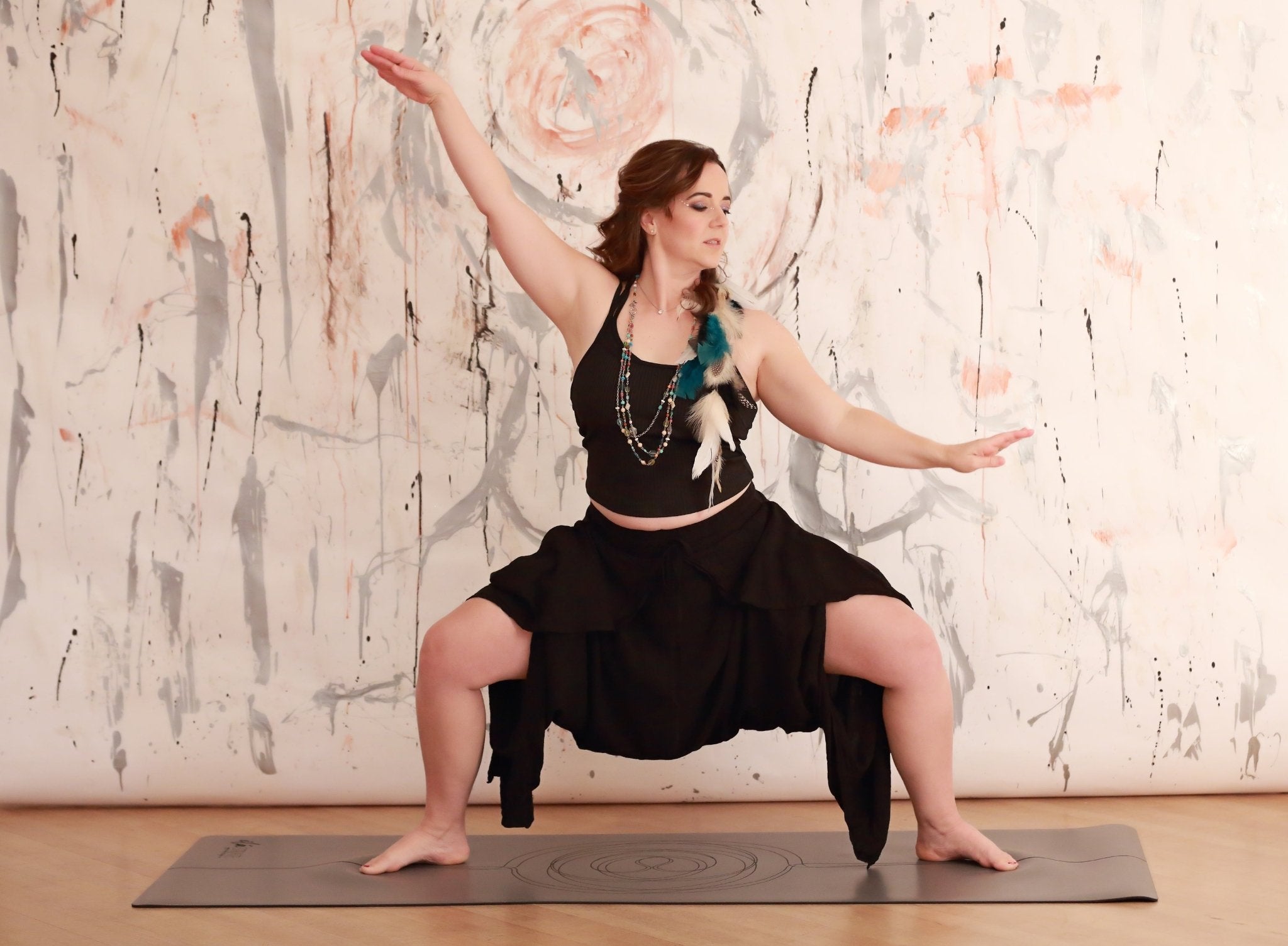 woman in warrior pose moving arms using grey yoga mat with sacred geometry design