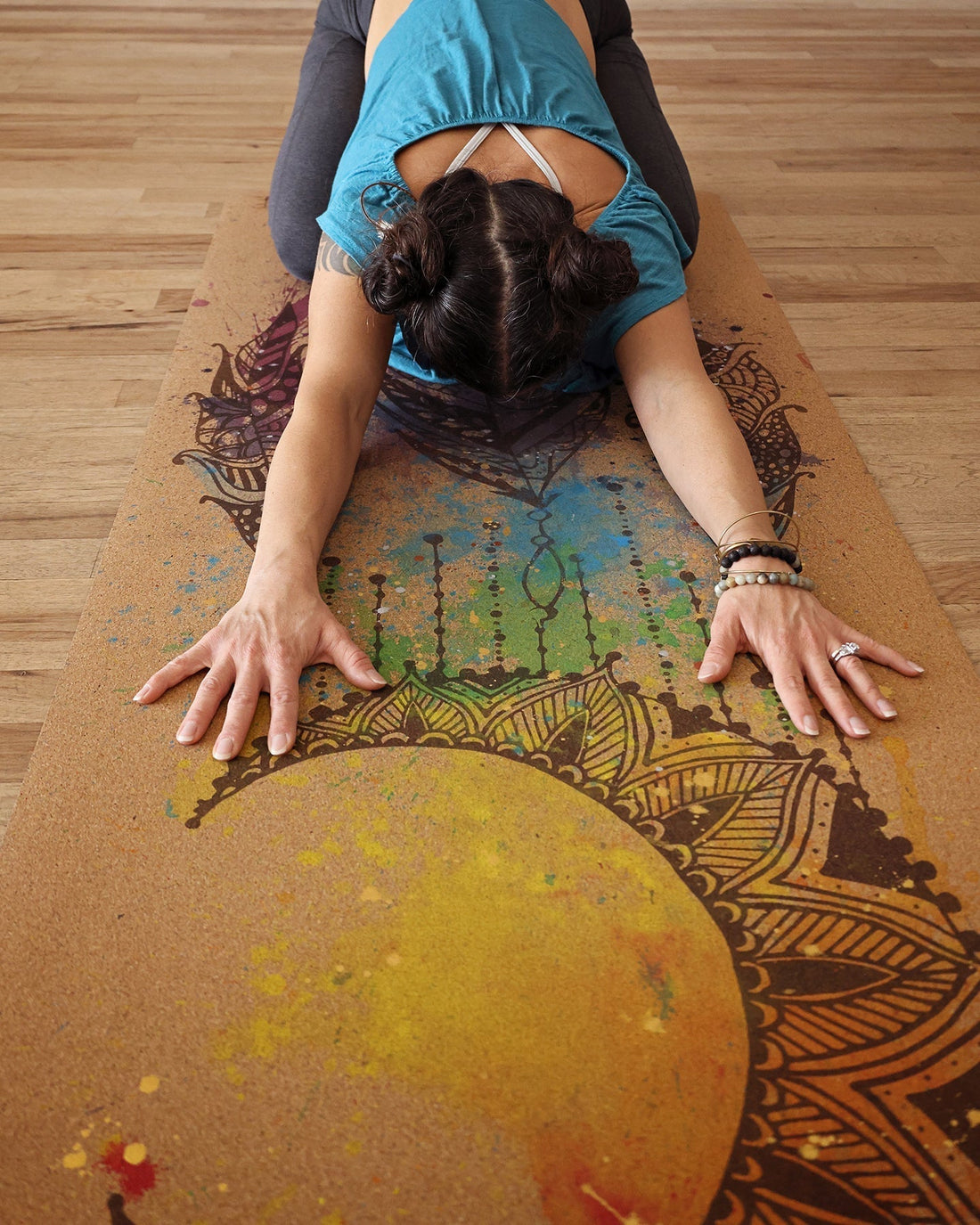 yogi on beautiful mandal chakra yoga mat. Cork yoga mat features hand painted design using splatter paint with chakra colors.