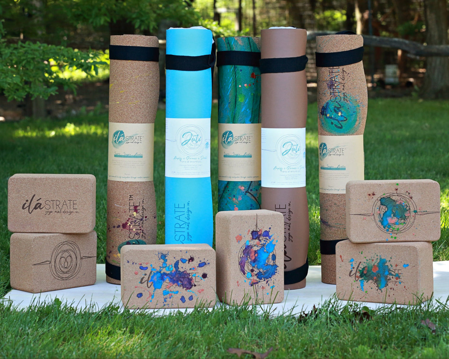 Yoga mats and cork yoga blocks with 'ilaSTRATE' branding on a grassy background