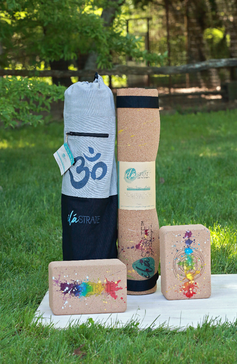 Yoga accessories including a colorful yoga mat, set of chakra rainbow colored cork yoga blocks, and yoga mat bag on a grassy background