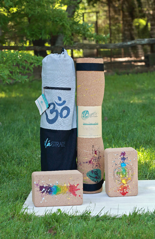 Yoga accessories including a colorful yoga mat, set of chakra rainbow colored cork yoga blocks, and yoga mat bag on a grassy background