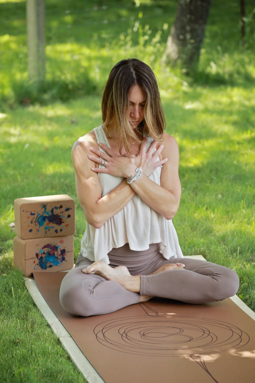 Woman practicing yoga on a brown yoga mat outdoors with cork yoga blocks and colorful mat design.